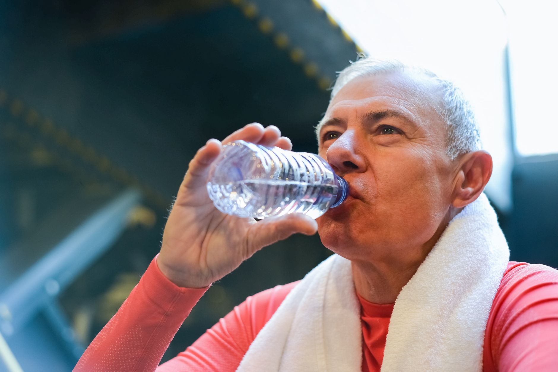 elderly man in red shirt drinking water from a plastic bottle